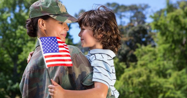 Military mother in uniform holding her young son who is holding an American flag