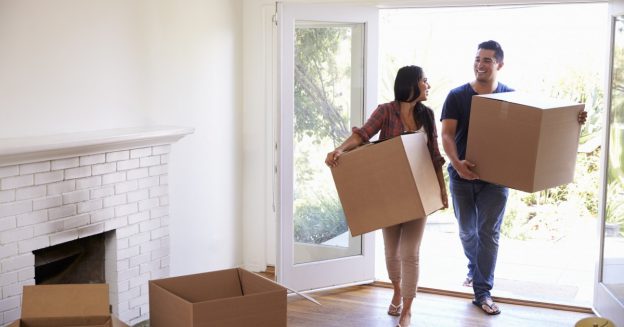 Smiling couple (female & male) moving into empty home, holding boxes