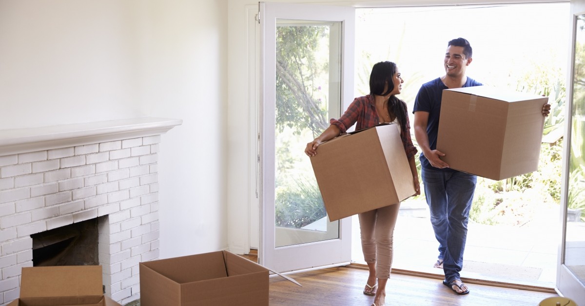 Smiling couple (female & male) moving into empty home, holding boxes