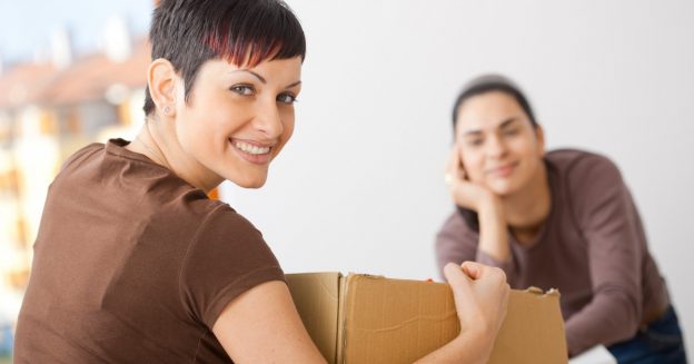 Two women smiling at the camera while moving brown boxes