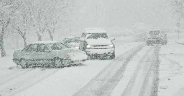 Four passenger vehicles on the road during a hazardous snow storm.