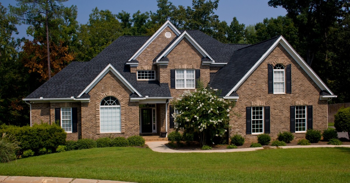 Front view of a two-story residential home with gables, manicured green lawn and driveway.